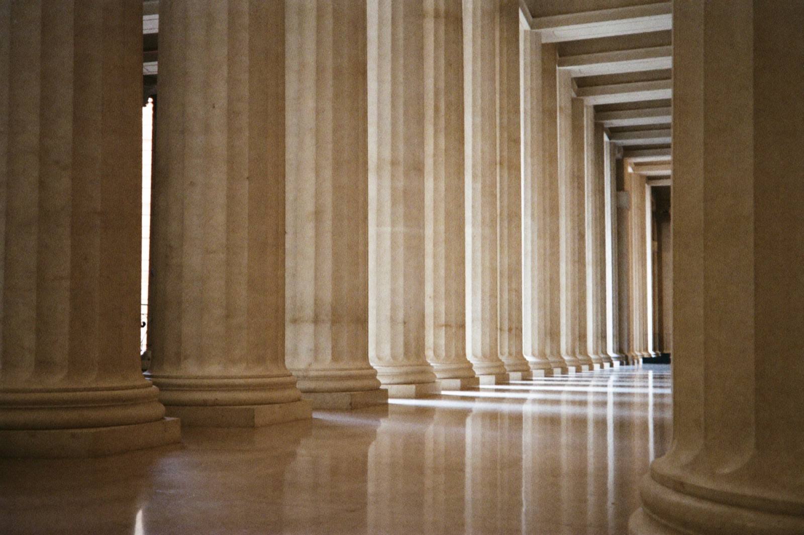 A long colonnade of pale stone columns receding in even rhythm, lit by soft daylight.